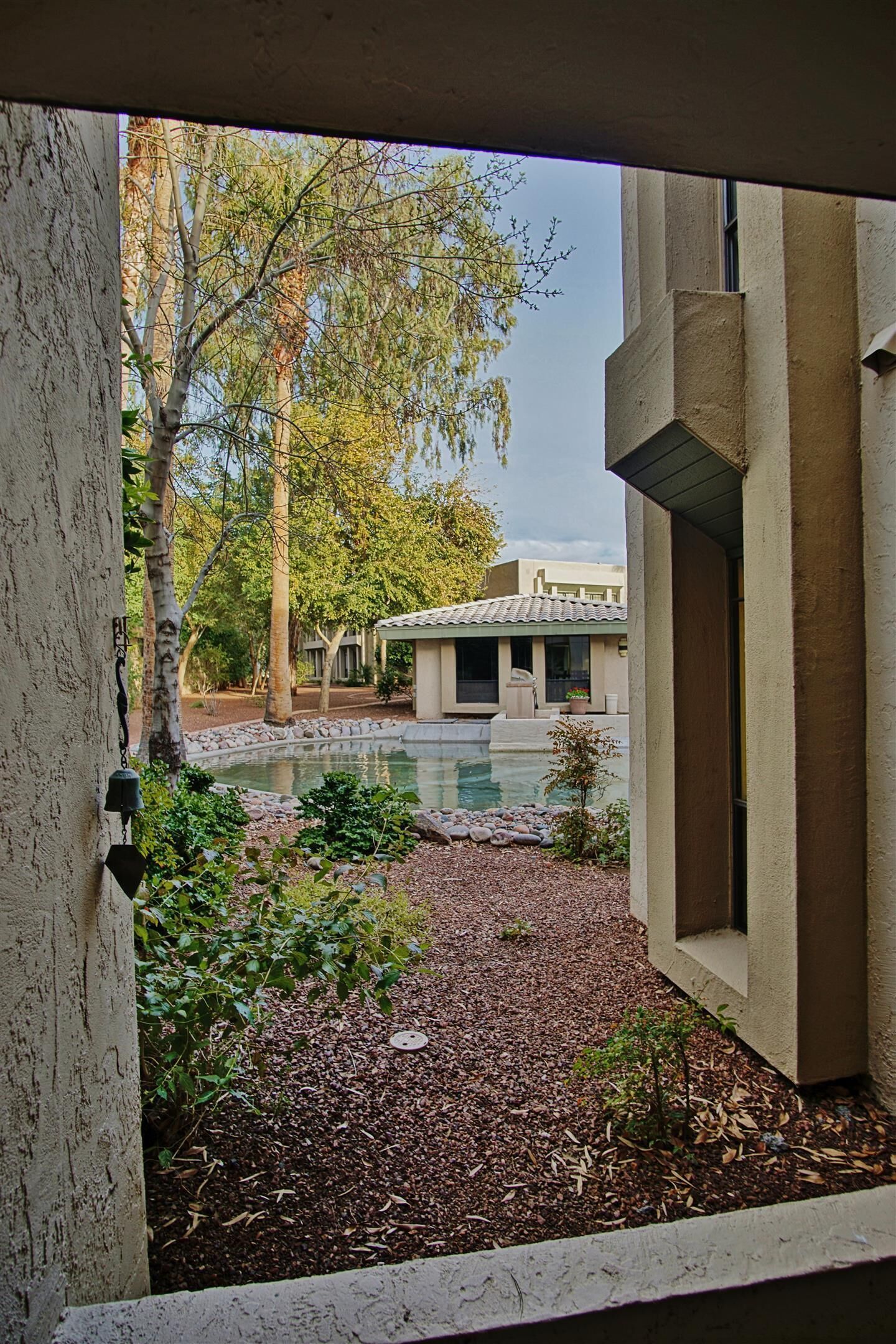 Une vue d’une cour avec une piscine, entourée d’arbres et d’un bâtiment dont le toit est recouvert de tuiles.