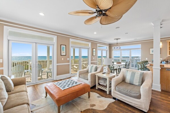A spacious living room with a large sliding glass door leading to a balcony, a ceiling fan, and a dining area with a table and chairs.