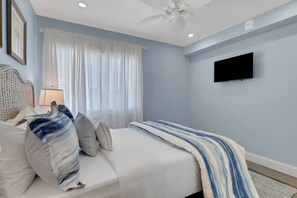 A bedroom with a bed, a television, a ceiling fan, and a window with curtains.