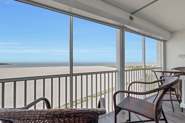 A balcony with wicker chairs, a railing, and a view of the beach and ocean.