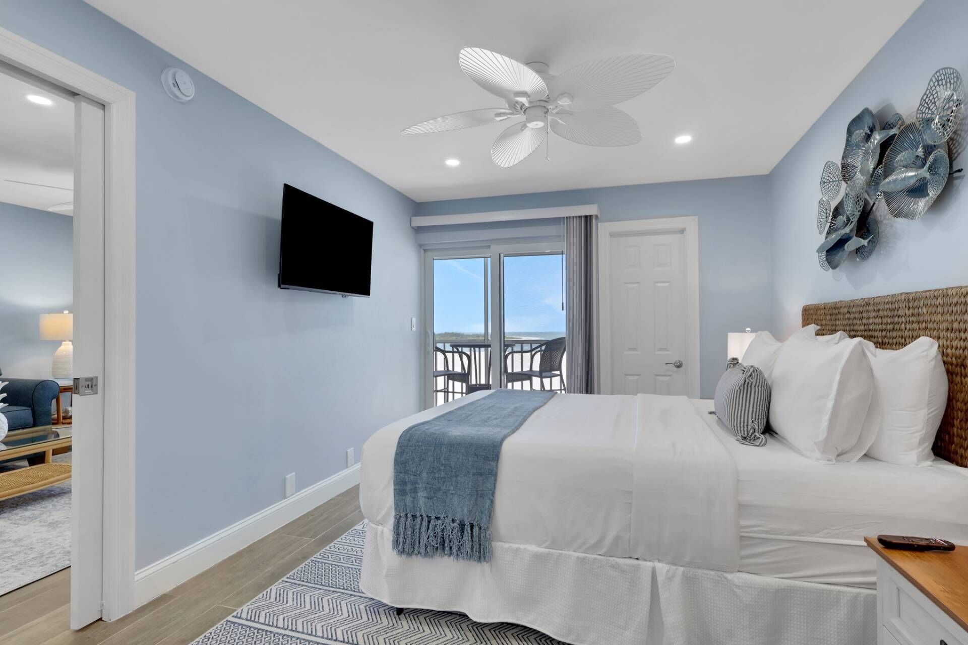 Camera da letto con un letto, una ventola a soffitto, una televisione e un balcone con sedie.