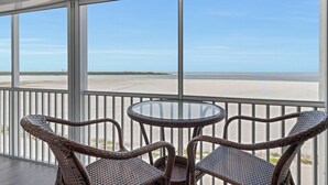 A balcony with wicker chairs and a glass table, overlooking a beach with a clear sky. - Beautiful Condo! Spectacular Gulf View! Huge Private Beachfront, Heated Pool, Free Wifi & Parking! (Fort Myers Beach)