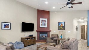 A living room with a fireplace, a television, and a ceiling fan. - Home Downtown | Indoor Pool | Fenced Backyard (Moab)