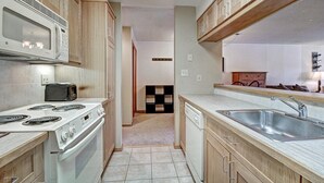 A narrow kitchen with wooden cabinets, a built-in microwave, a stove, a toaster, and a sink. - Spacious, Comfortable Retreat At Copper Mountain with available hot tub! VS549 (Copper Mountain)