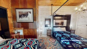 Una habitació amb un llit, una taula de treball i una cadira. Hi ha un quadre amb marc a la paret.