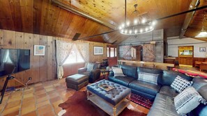 A cozy living room with a leather sofa, a television, and a wooden ceiling. - Pack Creek - The Lodge (Moab)