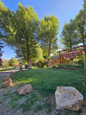 A ranch-style building with a sign indicating Pack Creek Ranch Desert Sanctuary, rental cabins, and a website. - Pack Creek - The Lodge (Moab)