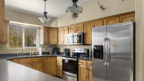 A kitchen with wooden cabinets, stainless steel appliances, a granite countertop, and a window with blinds. - Downtown Location | Indoor Pool | Fenced Backyard (Moab)