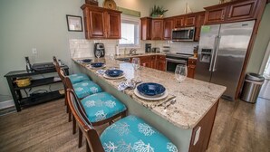 A kitchen with wooden cabinets, a granite countertop, and a built-in island with blue chairs. - La Bella Vita- Beautiful views of the gulf with private pool! (Port St Joe)