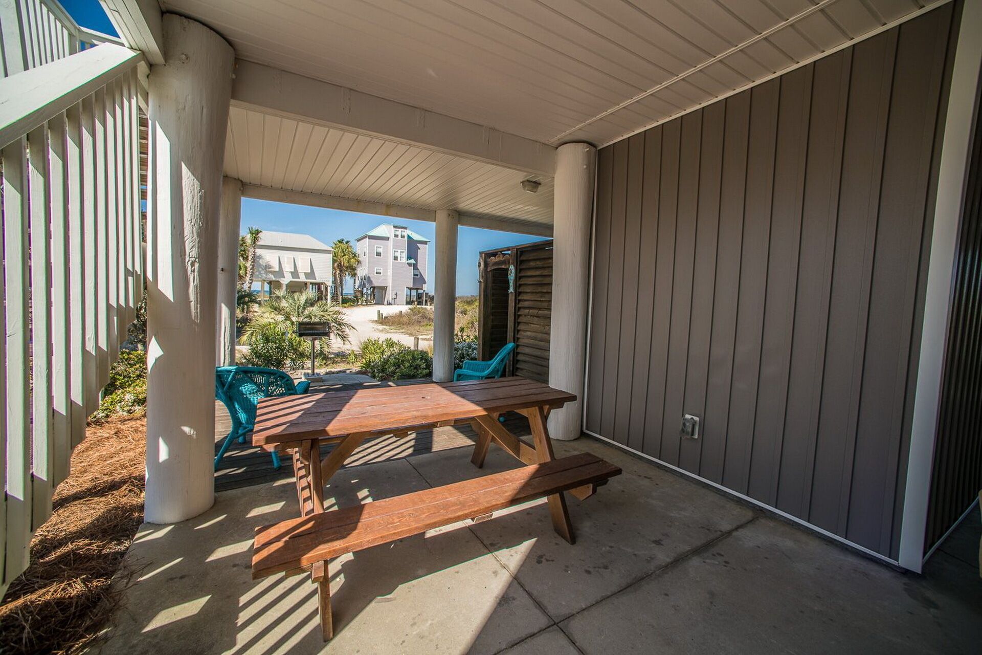 Une terrasse extérieure avec une table et des bancs en bois, entourée d’une zone abritée offrant une vue sur les bâtiments et un ciel dégagé.