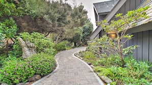A curved stone pathway leading to a building with a grey exterior and a sloped roof. - Spacious Redwood Retreat w/ Hidden Hot Tub (Manchester)