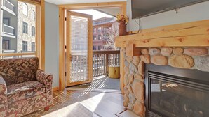Una sala de estar con chimenea de piedra, un sofá estampado y vistas a un balcón con paisaje urbano.