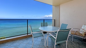 Un balcone con tavolo e sedie in vetro, vista su un mare azzurro e limpido.