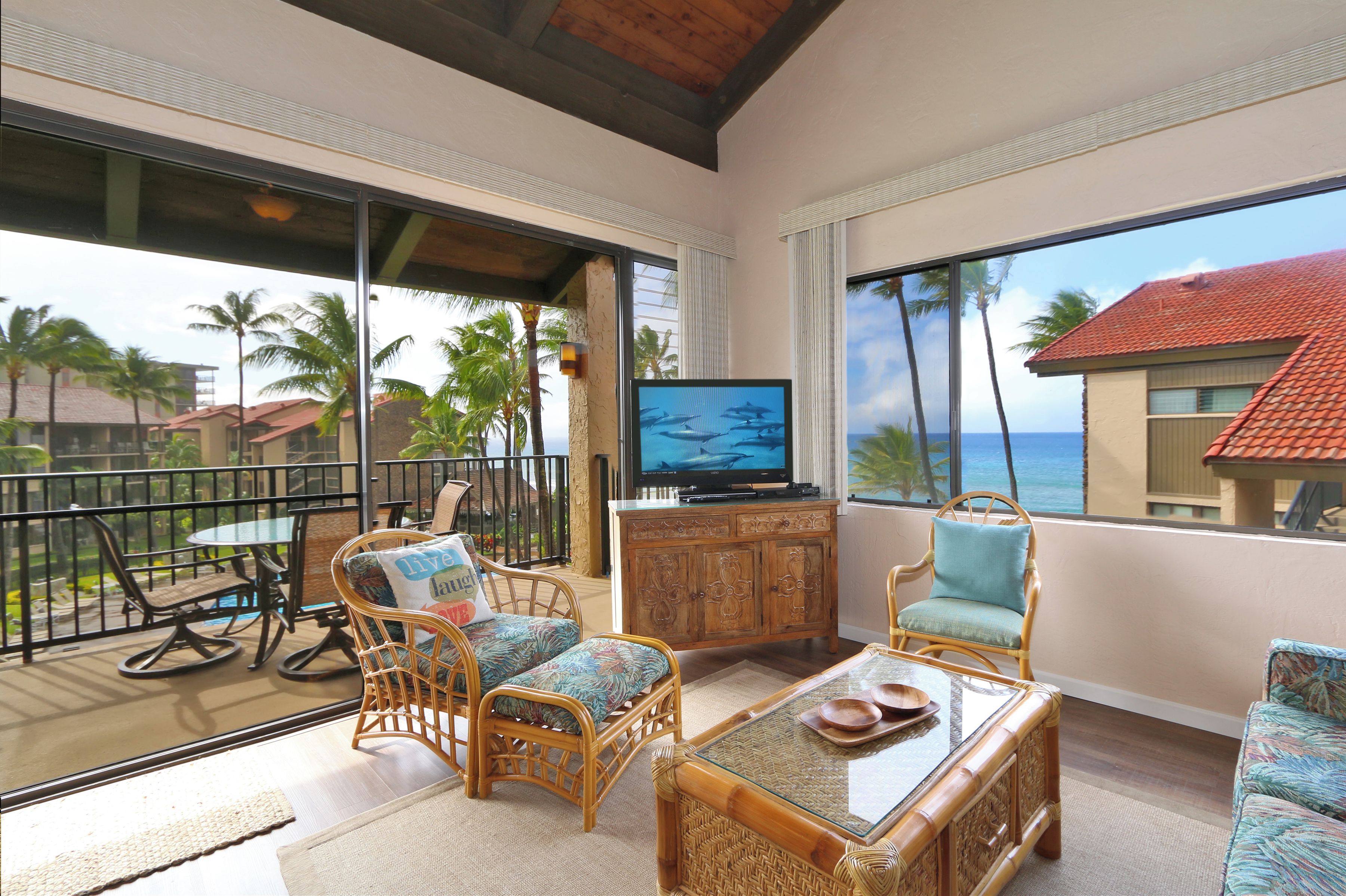 Ein Balkon mit Korbmöbeln, einem Fernseher und Blick auf das Meer.