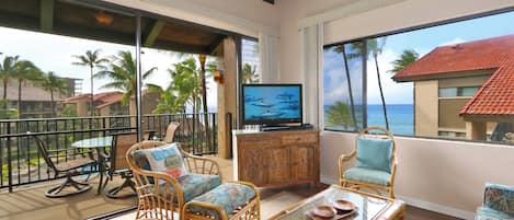 Ein Balkon mit Korbmöbeln, einem Fernseher und Blick auf das Meer.