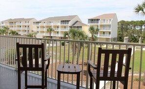 A balcony with two wooden chairs and a small table, overlooking a building with multiple balconies and a grassy area. - 4bdrm Townhome on N CSB (Cape San Blas)