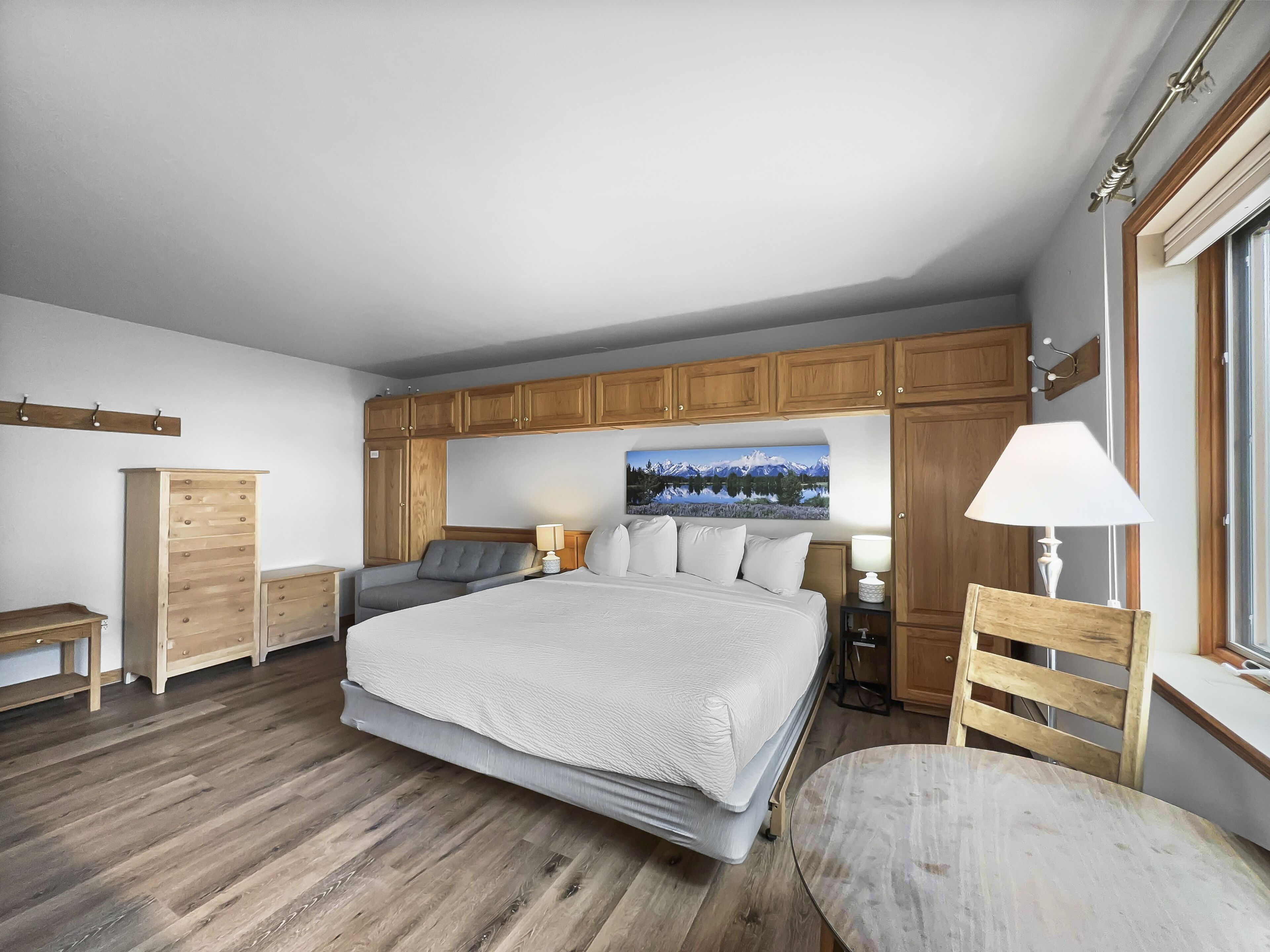 A bedroom with a large bed, wooden cabinets, a desk, and a chair.