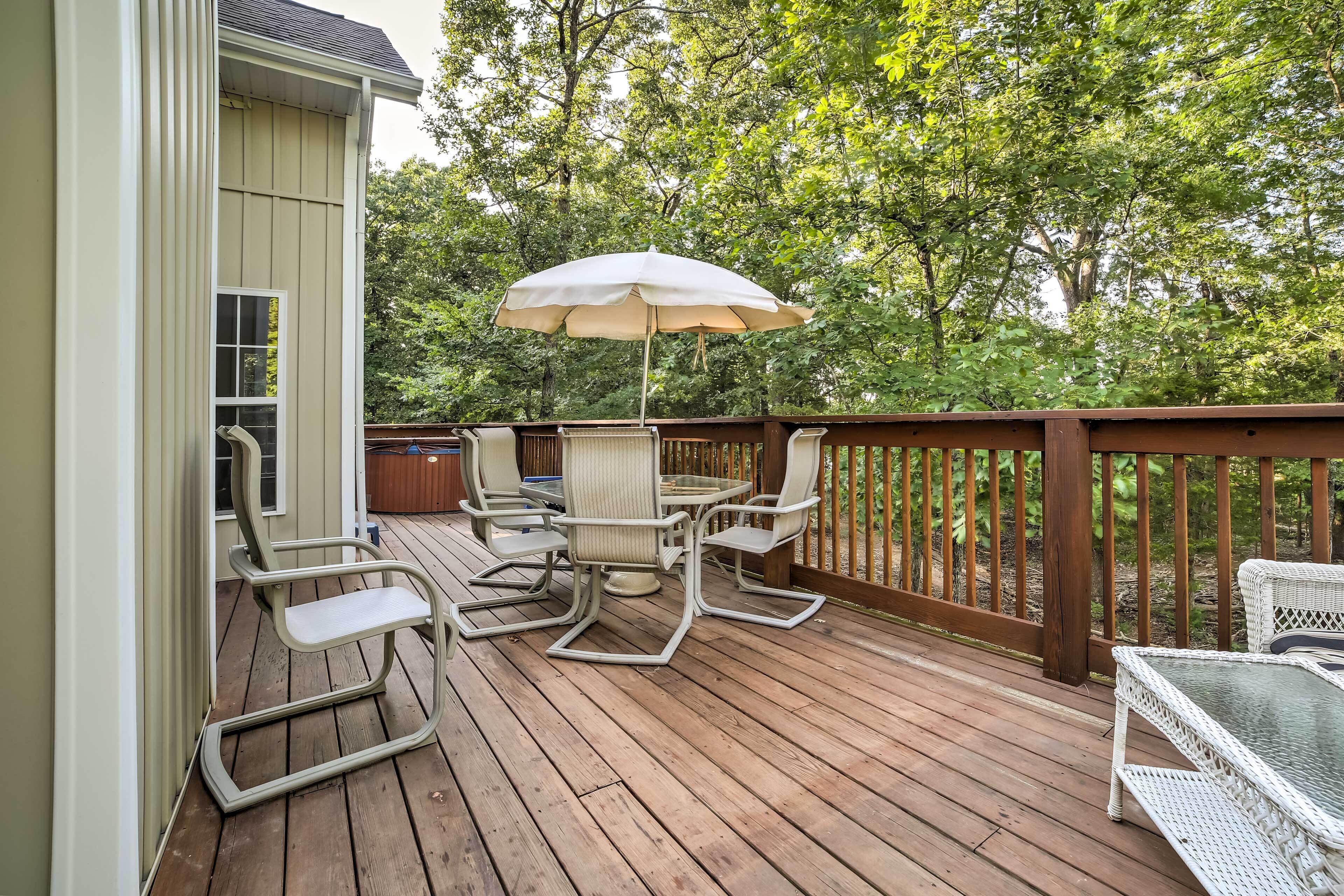 Une terrasse en bois avec une table et des chaises, un parasol et une vue sur les arbres.