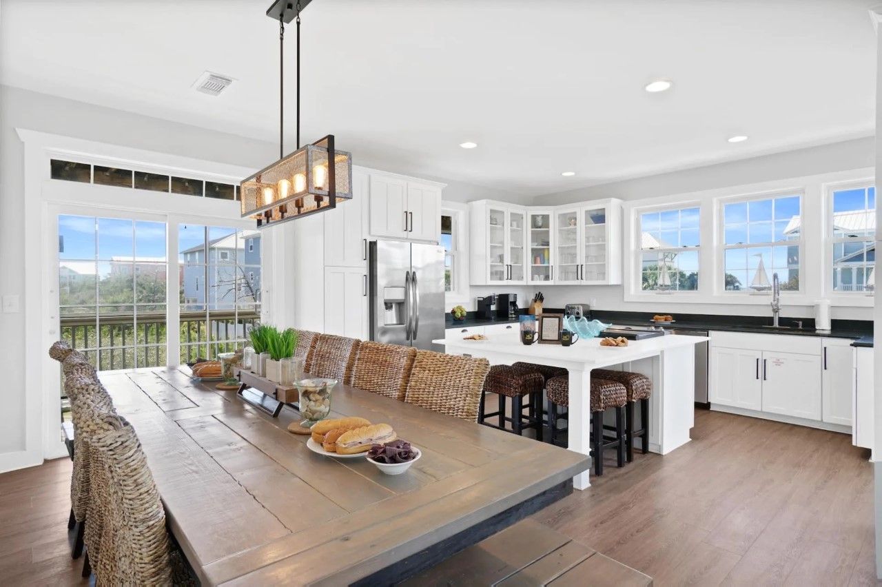 A spacious kitchen with white cabinets, a large island, and a dining area with a wooden table and wicker chairs.