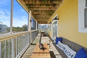 Un balcon abrité avec une table en bois, un banc et un coussin orné du mot « BEACHACH ».
