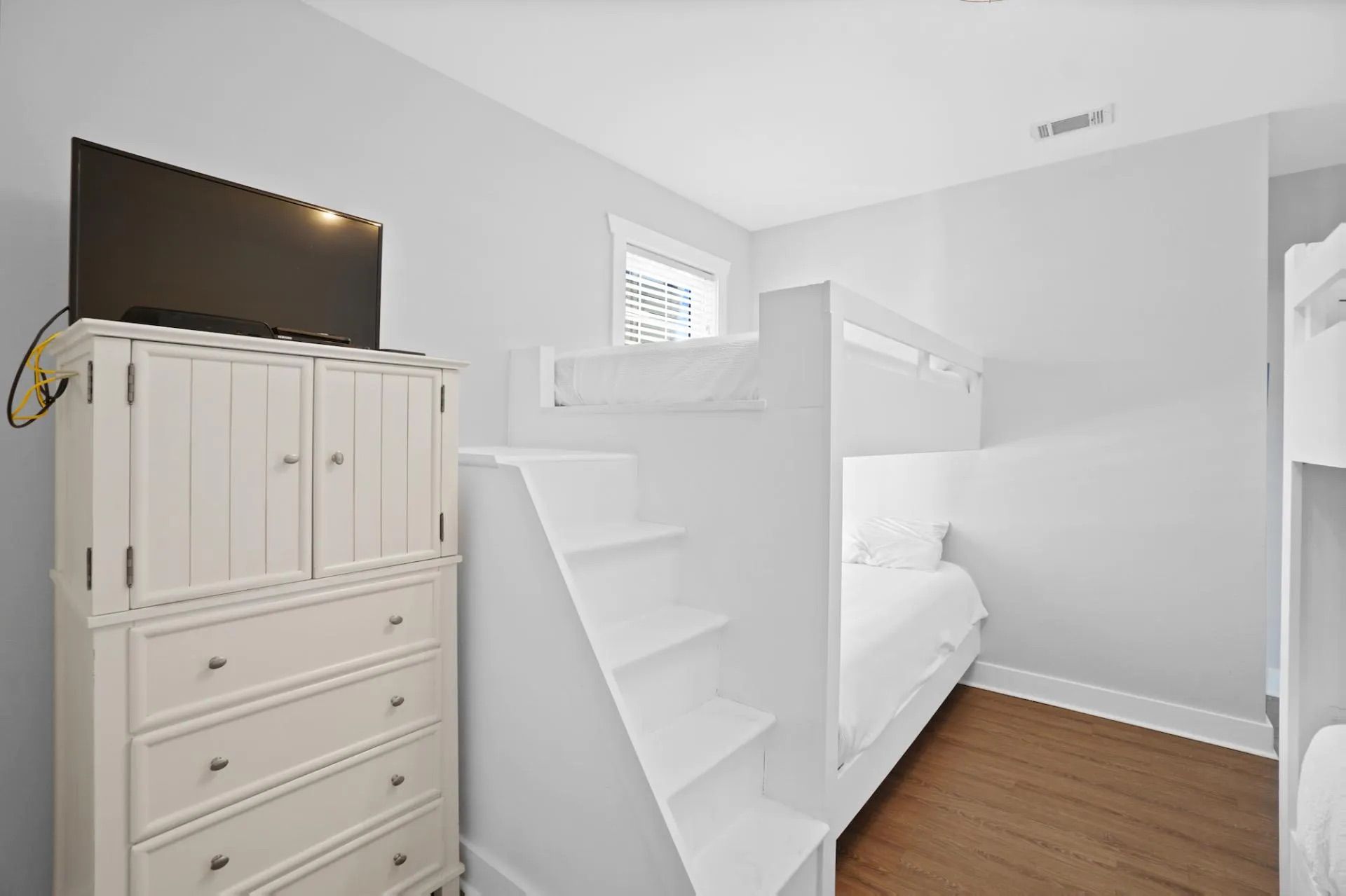 A bedroom with a bunk bed, a white wardrobe, and a small window.