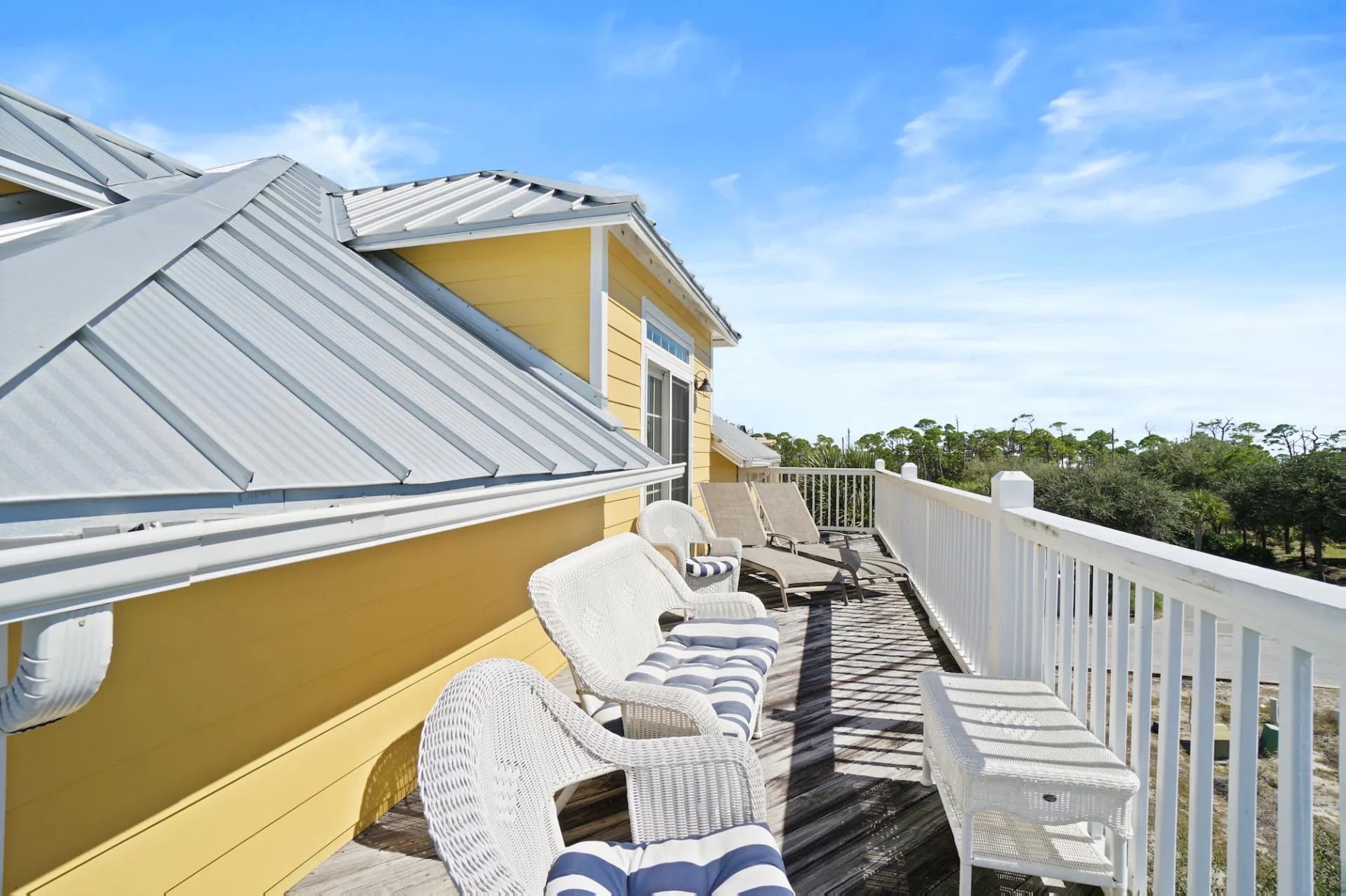 A covered outdoor deck with wicker furniture and a white railing, overlooking a natural landscape.
