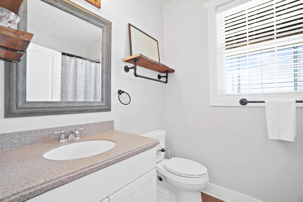 A bathroom with a white sink, a toilet, a mirror, and a window with blinds.