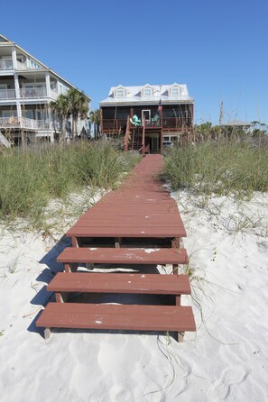 A wooden boardwalk leading to a beach house with a balcony and an American flag.