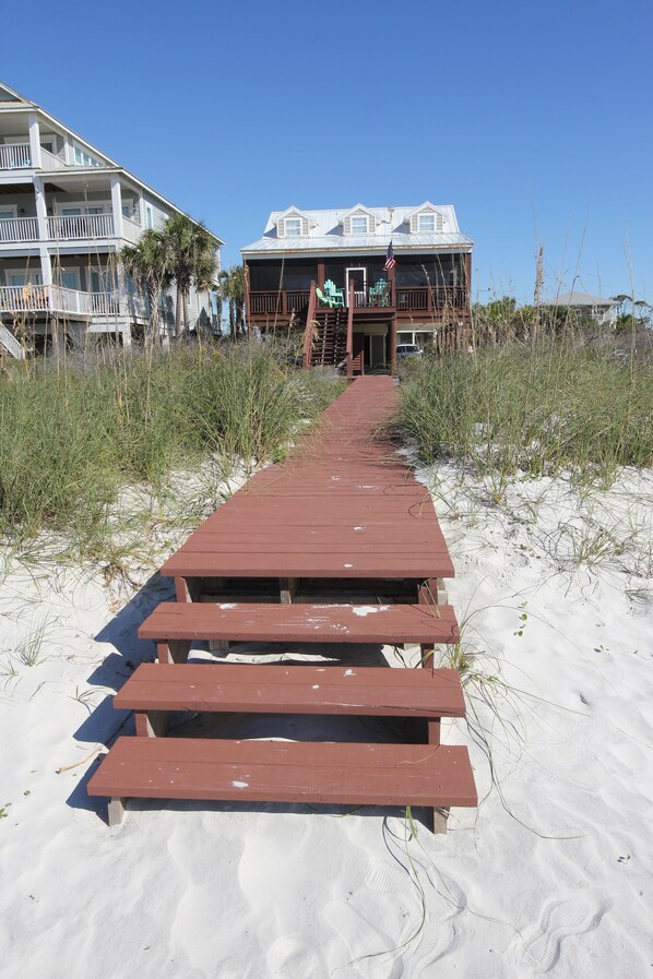 A wooden boardwalk leading to a beach house with a balcony and an American flag. - Beach Front Fun & Relaxation (Port St Joe)
