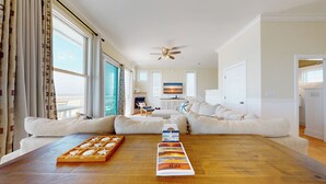 A spacious living room with a large sectional sofa, a wooden coffee table, and a view of the ocean through large windows. - Casual Beach Front with New Owners: Lots of updates! (Cape San Blas)