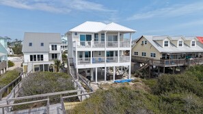 A multi-story beachfront property with a balcony, a covered deck, and a staircase leading to the upper levels.