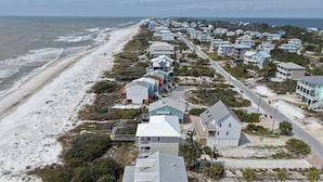 A coastal residential area with houses along the beach, featuring a mix of single and multi-story buildings, some with balconies and a few with attached garages. - Casual Beach Front with New Owners: Lots of updates! (Cape San Blas)