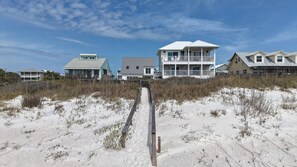 A beachfront property with a sandy path leading to a multi-story building with balconies.