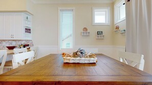 A dining room with a wooden table, white chairs, a basket with decorative items, and a brick backsplash.