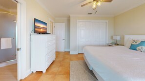 A bedroom with a bed, a dresser, a television on the dresser, a ceiling fan, and a door.