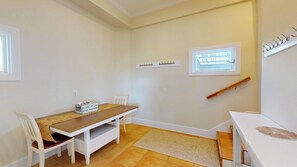 A dining area with a wooden table and white chairs, a small rug, and a window with a view.