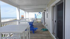A covered outdoor area with a white table and blue chairs, overlooking the beach.