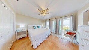 A bedroom with a bed, a nightstand, a chair, a ceiling fan, and a view of the outdoors.