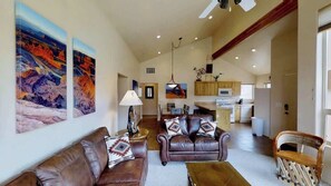 A spacious living room with a brown leather sofa, a wooden coffee table, and a dining area with wooden cabinets and a kitchen in the background. - La Sal Overlook - S3, Best Views in Rim Village (Moab)