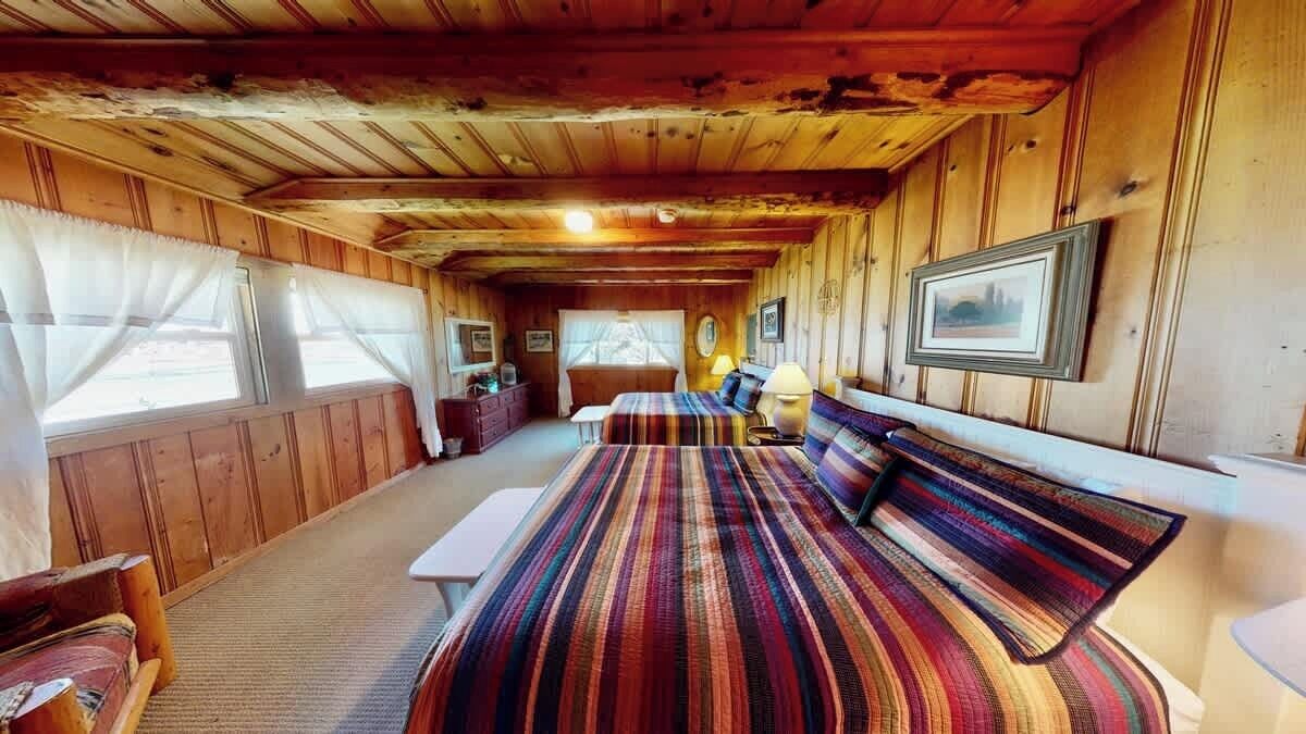 A wooden cabin interior with a bed, a bench, and a window.