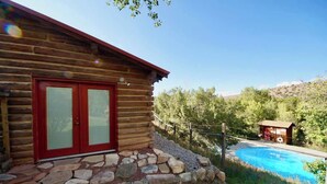 A log cabin with a red door and a stone foundation. - Pack Creek - Ranch House, Hot Tub, Sauna, Cabin (Moab)