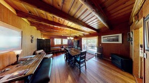 A wooden interior with a long dining table, benches, and a fireplace.