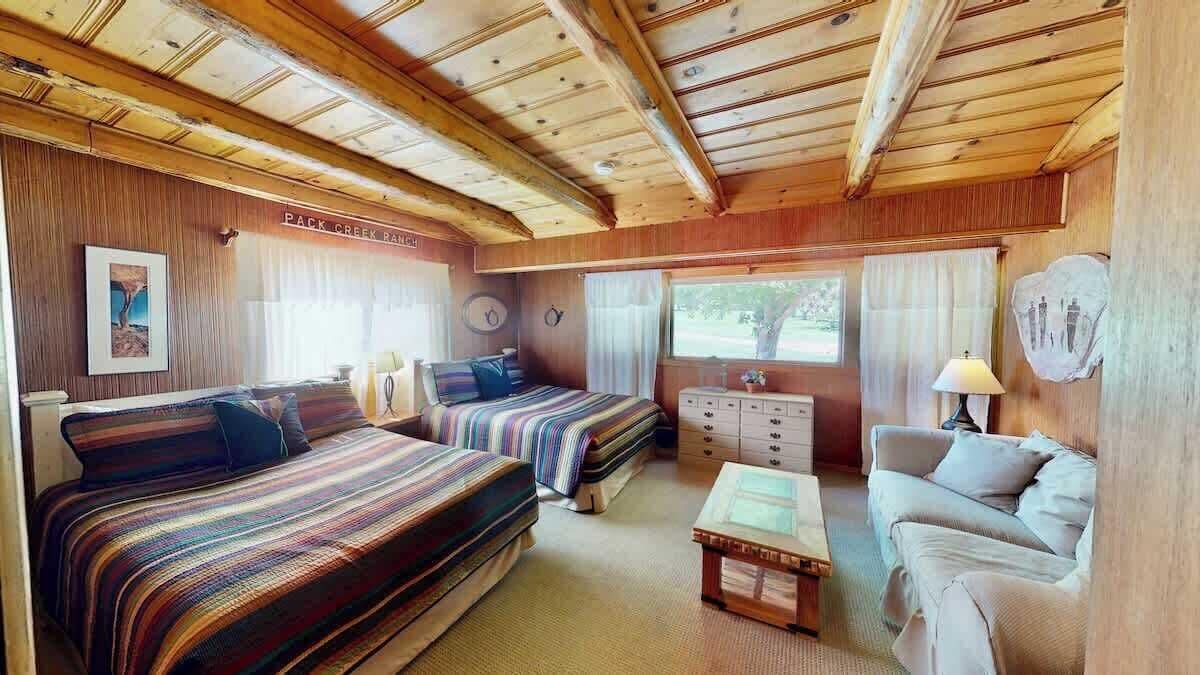 A cabin interior with two beds, a sofa, a table, and a window with curtains.