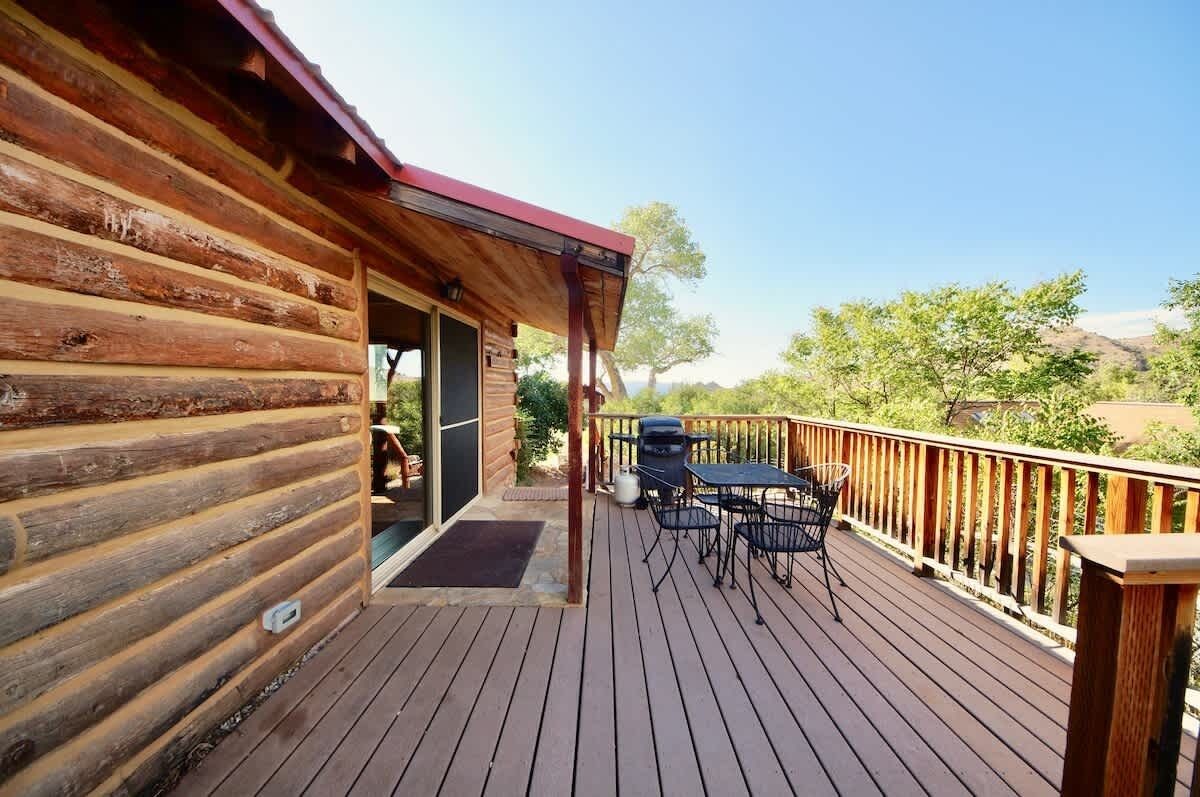 A wooden cabin with a deck, outdoor seating, and a view of the surrounding landscape.