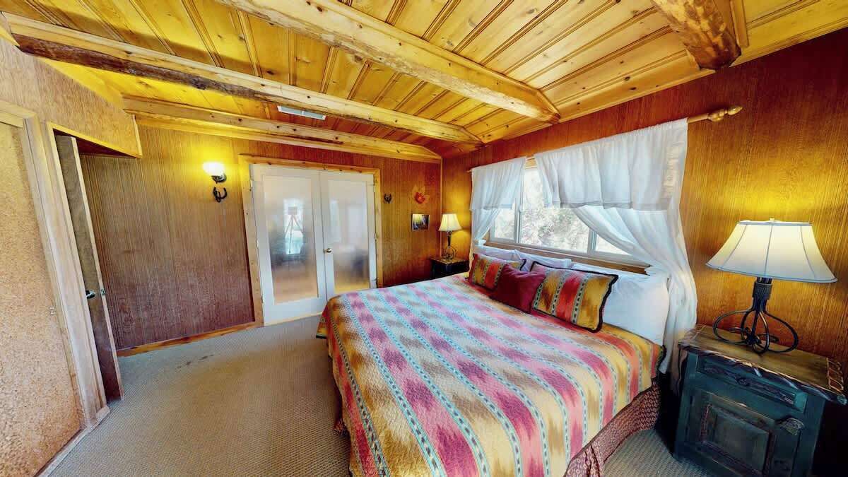 A bedroom with a bed, bedside lamps, a window with curtains, and a wooden ceiling.