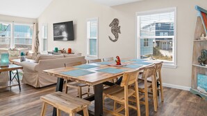 A dining area with a wooden table and chairs, a sofa, and a television on the wall. - 2 minute walk to the beach, stores and restaurants (Cape San Blas)