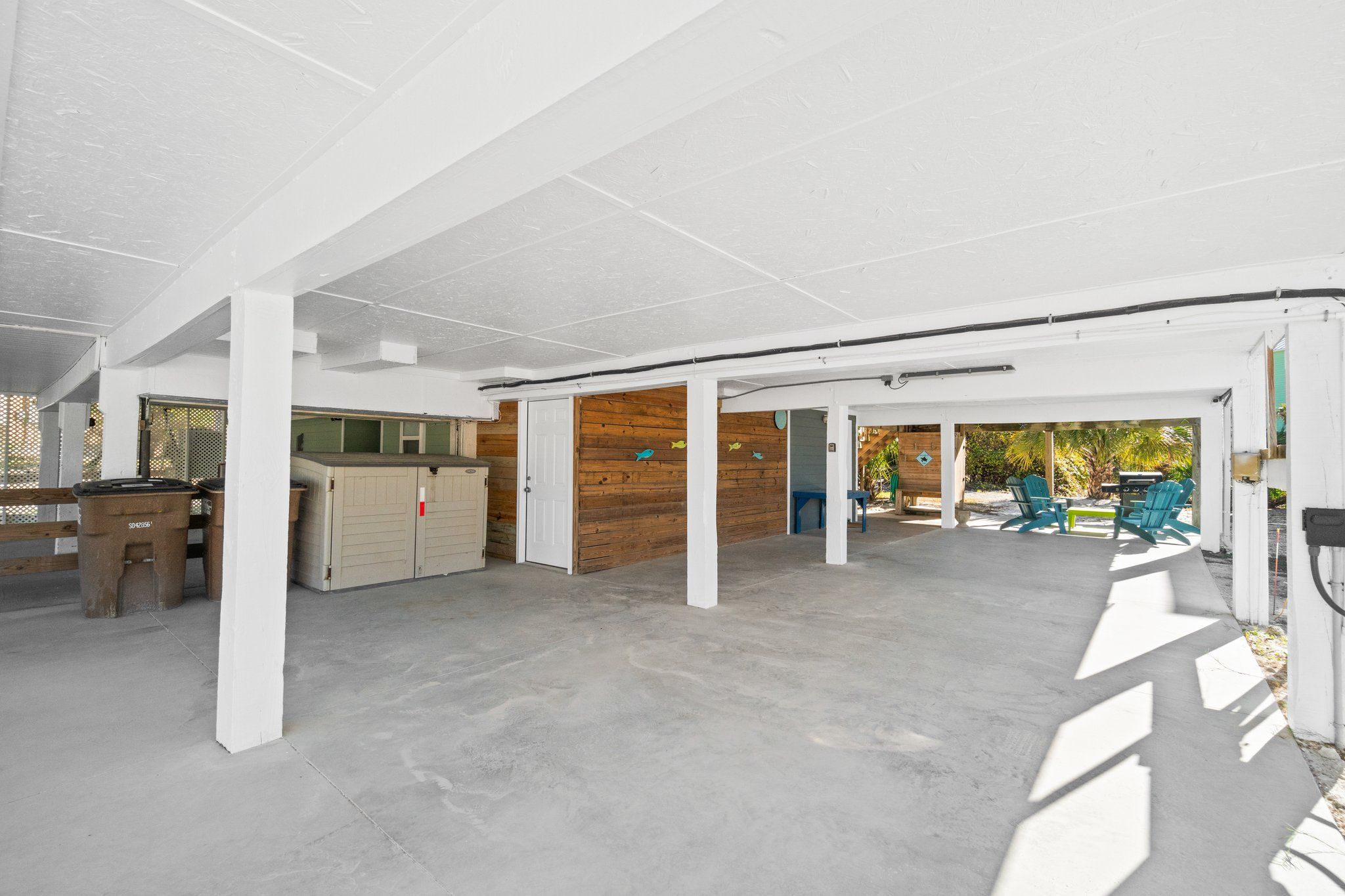 Un vaste espace intérieur doté d’un sol en béton, de piliers blancs et de murs en bois. Des espaces extérieurs aménagés avec des chaises et des tables sont également disponibles.