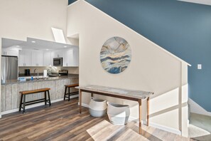 A modern kitchen with white cabinets, a marble countertop, and a wooden bench. There is a painting on the wall and a staircase leading to another level. - 2 minute walk to the beach, stores and restaurants (Cape San Blas)