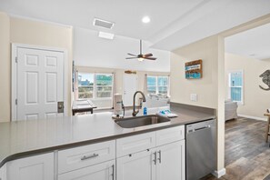 A modern kitchen with a large island, built-in dishwasher, and a ceiling fan.