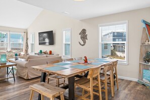 A dining area with a wooden table and chairs, a sofa, and a television on the wall.